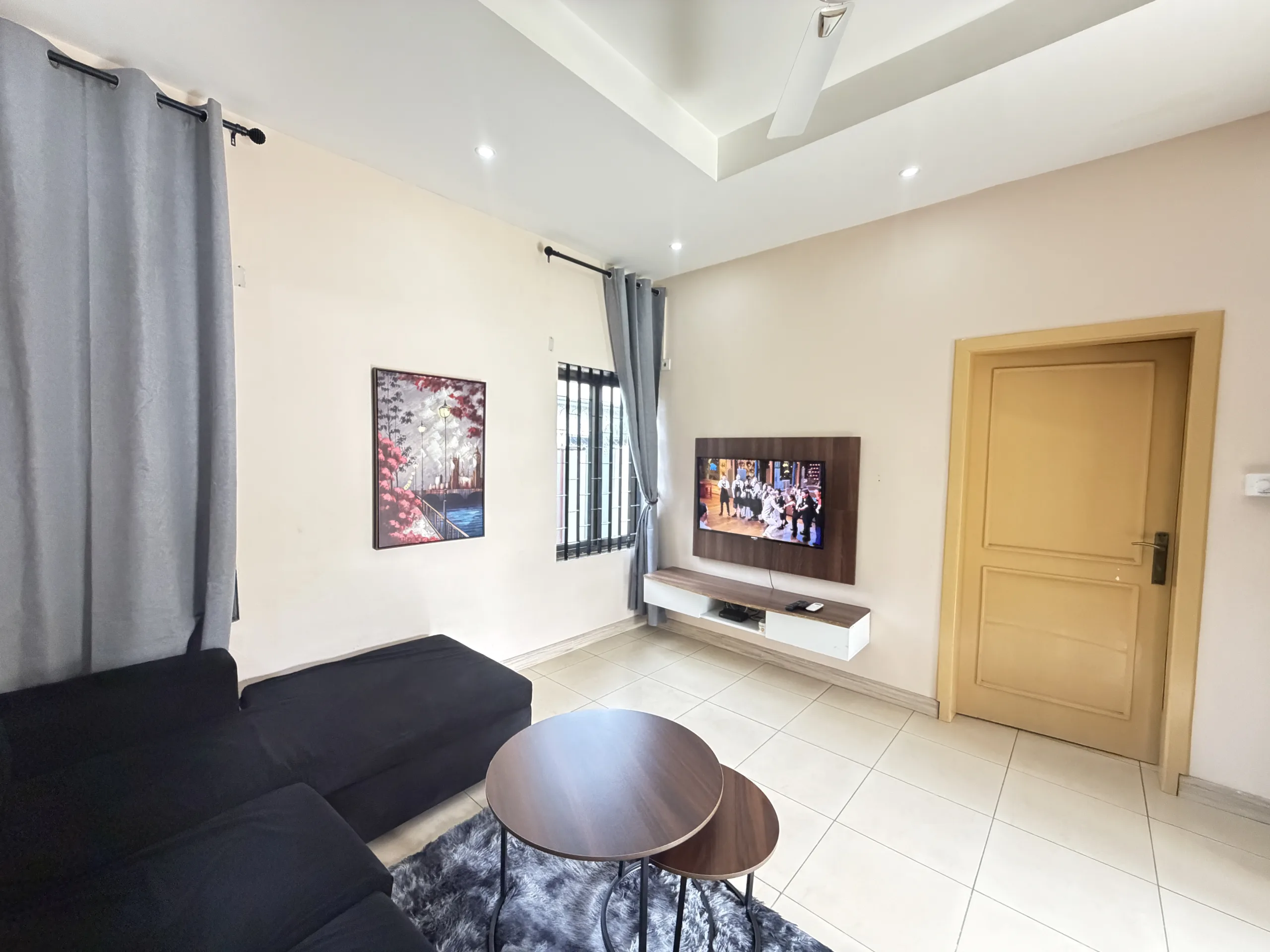 A wall-mounted television on a walnut panel, facing the corner sofa